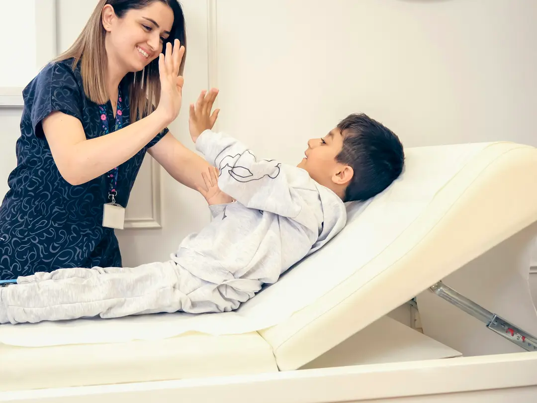 A nurse in a bright clinic room gives a young patient a high five.