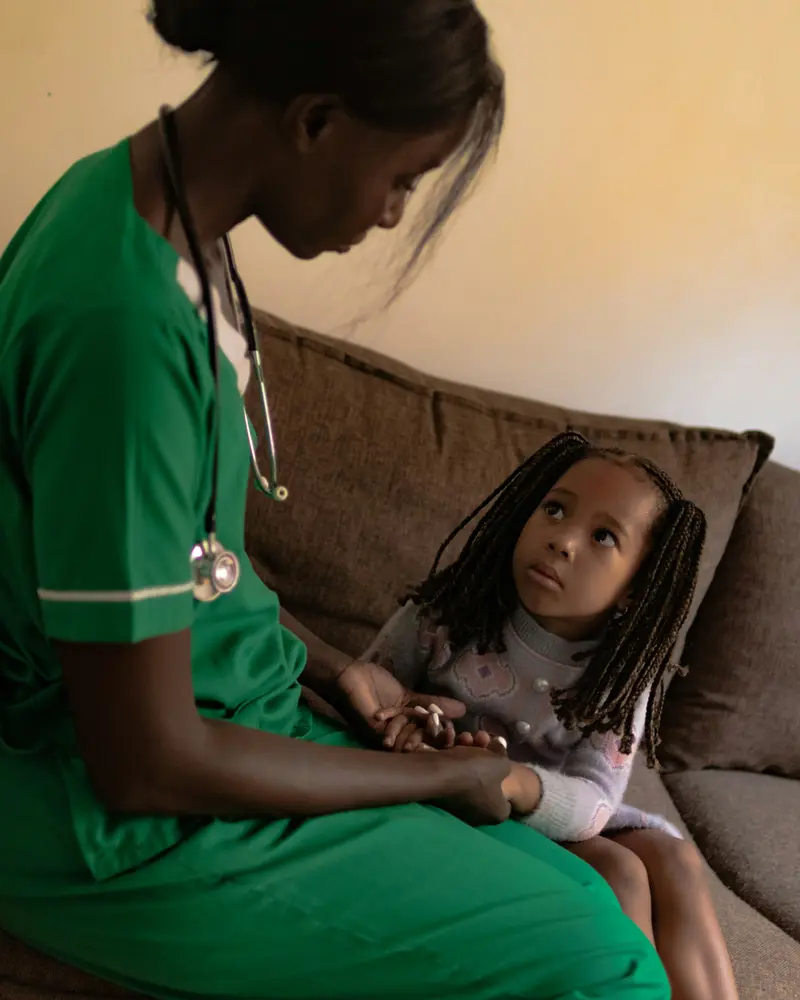 A nurse sits with a young girl and holds her hands.